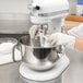 A woman wearing gloves using a KitchenAid mixer to mix ingredients in a bowl.