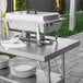 A Regency stainless steel folding work table with a chafing dish on it.