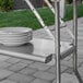 A Regency stainless steel folding work table with a stack of plates on it.