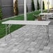 A Regency stainless steel folding work table on a stone walkway.
