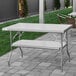 A Regency stainless steel folding table with a metal bar underneath on grass.