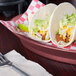 A table with a plate of tacos served on a HS Inc. raspberry oval deli server with a short base.