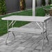 A Regency stainless steel folding work table with a metal bar on a brick patio.