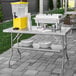 A Regency stainless steel folding work table with plates and a yellow container on it.