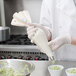A person wearing gloves using an Ateco canvas pastry bag to pipe food.