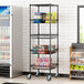 A Regency black wire shelving cart with baskets and a shelf holding snacks.