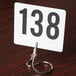 An American Metalcraft stainless steel alligator clip holding a white card with black numbers.