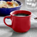 A red Tuxton round china cup filled with a drink on a table next to a blue bowl of food.