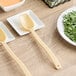 A white table with a plate of green leaves and a beige Cambro Camwear salad bar spoon.