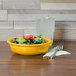 A yellow Fiesta china bowl filled with salad on a table.