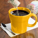 A yellow Fiesta tapered china mug on a counter with a liquid in it.