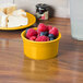 A Fiesta Daffodil china ramekin filled with raspberries and blueberries on a white table.