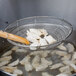 A person using the Town Fine Mesh Stainless Steel Skimmer with a bamboo handle to fry food.