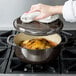 A woman using a white towel to clean a Lodge Midnight Chrome enameled cast iron Dutch oven on a stove.