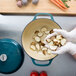 A person in gloves using a Lodge Lagoon Enameled Cast Iron Dutch Oven to cook potatoes.