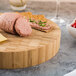 An American Metalcraft bamboo round cutting board with meat and cheese on it.