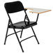 A black National Public Seating folding chair with a gray tablet arm.