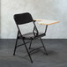 A black folding chair with a gray desk attached.