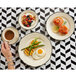 A woman's hand holding a cup of coffee on a Homer Laughlin black scalloped plate next to food.