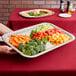 A person holding a Vollrath rectangular fluted stainless steel tray of vegetables and fruits.