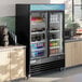 An Avantco swing glass door refrigerator with drinks and beverages inside.