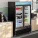 A black glass door merchandiser refrigerator with LED lighting, stocked with drinks and food items.