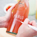 A person writing "Mango" on a white glass bottle with a Franmara neon white mini tip marker.