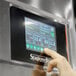 A hand pressing a button on the Stagionello meat curing cabinet with a digital display screen.