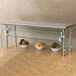 A stainless steel food shield on a counter with bowls of fruit on a shelf.