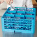 A person pouring water into a blue Carlisle glass rack on a counter.