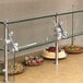 An Advance Tabco glass food shield on a counter with plates of desserts.