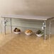 An Advance Tabco stainless steel food shield on a counter with bowls of fruit on a shelf.