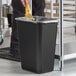 A hand holding a banana peel over a black Lavex rectangular trash can.
