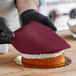 A person wearing black gloves cutting a Satin Ice burgundy cake.