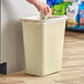 A hand putting a plastic bag into a white Lavex rectangular trash can.