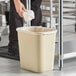 A person putting a paper towel in a Lavex beige rectangular trash can with a plastic bag inside.