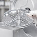 A gloved hand holds a Robot Coupe 5/64" metal grating / shredding disc.