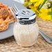 A Tablecraft chrome-plated slotted shaker top filled with powder next to a plate of spaghetti and meatballs.