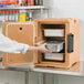 A woman using the front loading feature of a Cambro Ultra Pan Carrier in a kitchen.