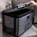 A hand opening a grey Rubbermaid ProServe food pan carrier bag.