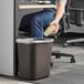 A man sitting in a chair in a corporate office putting a paper cup into a Lavex brown rectangular trash can.