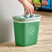 A hand putting a green Lavex recycling can into a white rectangular trash can.