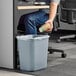 A man in a corporate office putting a coffee cup into a Lavex gray rectangular trash can.