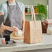 A woman in a grey apron using a brown Kraft paper bag with wooden handles.