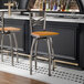 A metal bar stool with a cross back design and a cherry wood seat, featuring a swivel function.