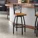 A black metal bar stool with a cross back design and a cherry wood seat.
