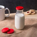 A close up of an Acopa red milk bottle lid on a glass bottle of milk.