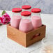 Acopa Red Solid Milk Bottle Lid on a group of Acopa milk bottles in a wooden crate.