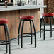 A row of Lancaster Table & Seating black swivel backless bar stools with maroon vinyl seats at a bar.