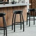 A row of Lancaster Table & Seating black swivel backless bar stools with black vinyl seats at a bar.